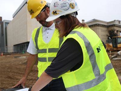 Two builders in safety vest and glasses at a construction site.